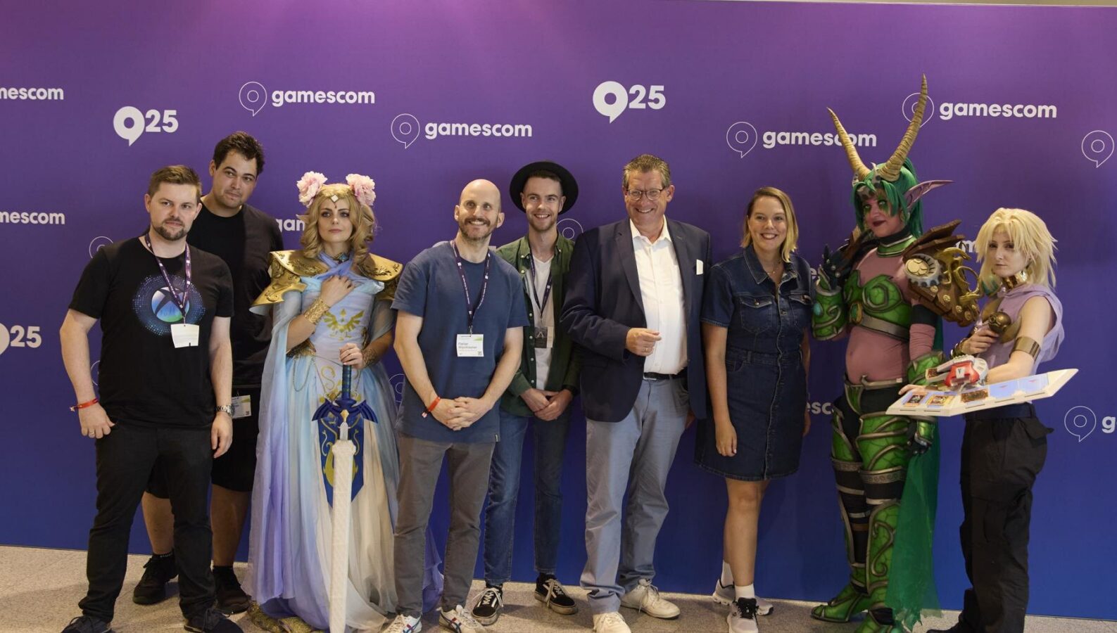 Gruppenfoto der LGA mit Dietmar Brockes (FDP, MdL NRW, im Sakko) und Cosplayern vor der Gamescom-Wand 2025